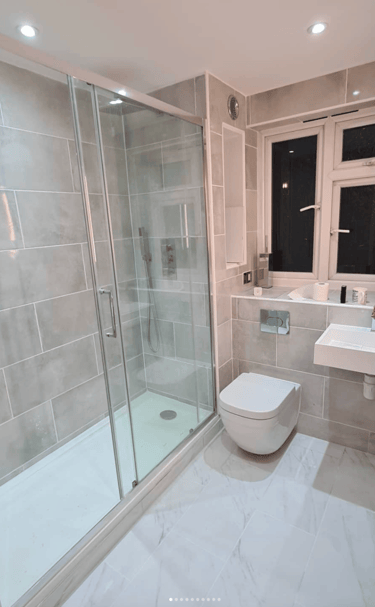 A fully renovated luxury bathroom featuring a large glass walk-in shower, wall-mounted toilet, and a