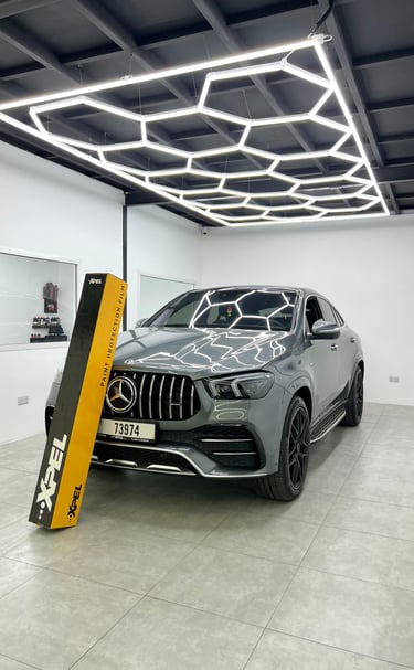 Grey Mercedes-Benz SUV in a detailing studio with XPEL paint protection film box and hexagon LED ceiling lights.