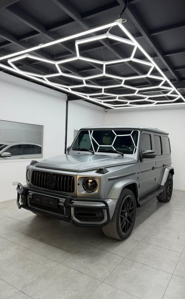 Silver Mercedes-Benz G-Class SUV parked in a garage with modern hexagonal LED ceiling lights.