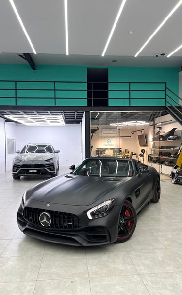 Matte black Mercedes-AMG GT Roadster and silver Lamborghini Urus in a modern luxury car detailing garage.