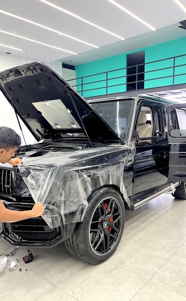 A technician applying clear paint protection film PPF to a black Mercedes-Benz G-Wagon SUV.