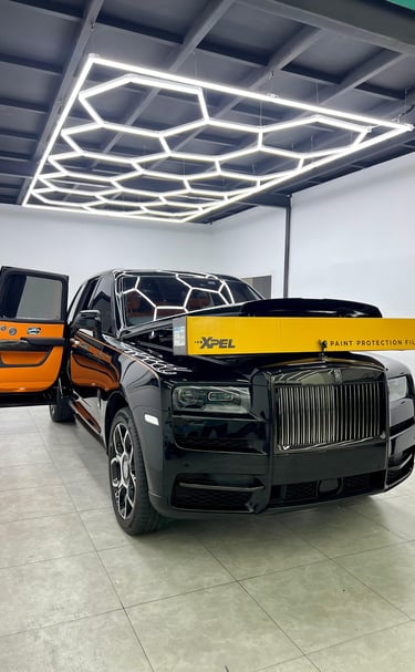 Black Rolls-Royce Cullinan receiving XPEL paint protection film installation in a detailing studio.