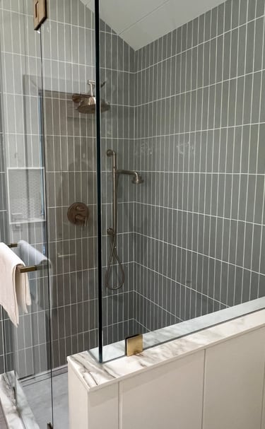 Modern walk-in shower with vertical grey subway tiles, frameless glass enclosure, and bronze hardware.