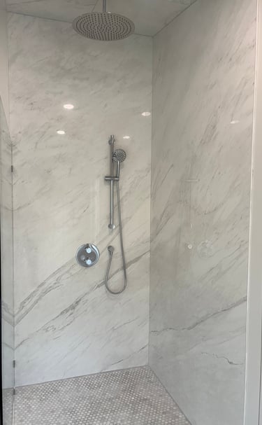 Luxury walk-in shower with white marble wall panels, rain shower head, and chrome handheld sprayer.