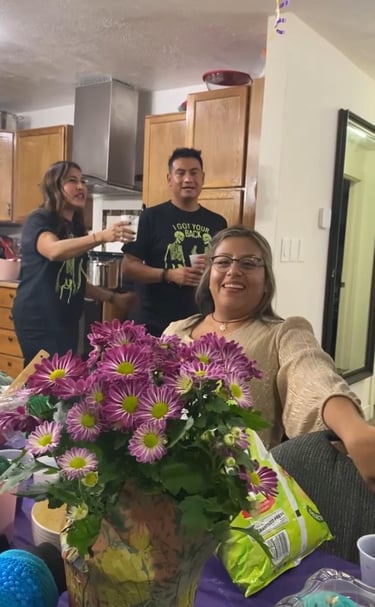 Friends celebrate at a house party with purple flowers, snacks, and drinks in a kitchen.