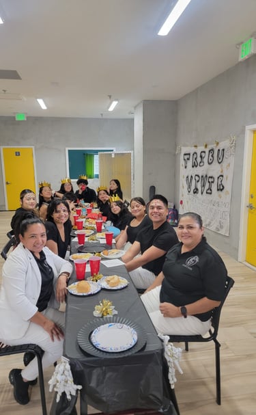 A diverse group of people celebrating at a long banquet table with food, party hats, and festive decor.