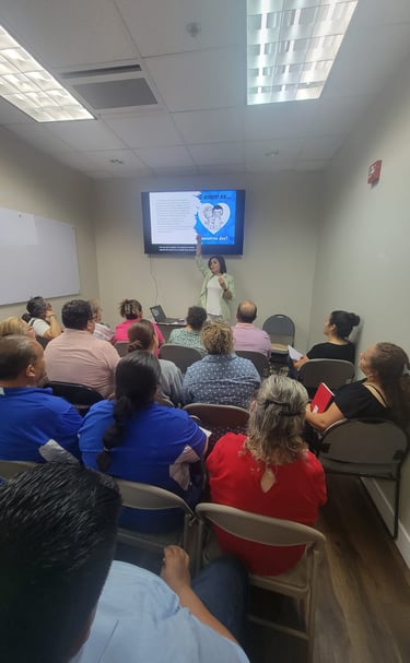 A group of people attending an educational workshop with a woman presenting slides on a digital screen.