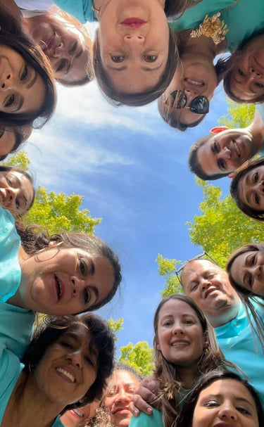 A diverse group of smiling people in teal shirts posing for a low angle circle selfie outdoors.