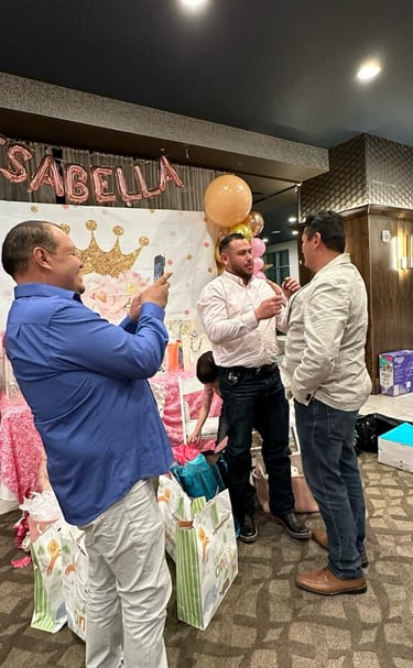 Three men celebrate at a pink princess themed first birthday party with balloons and gifts.