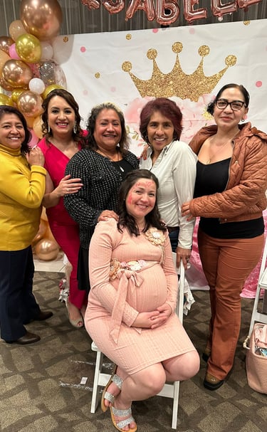 A group of happy women celebrate at a royal-themed baby shower with gold balloons and a princess crown backdrop.