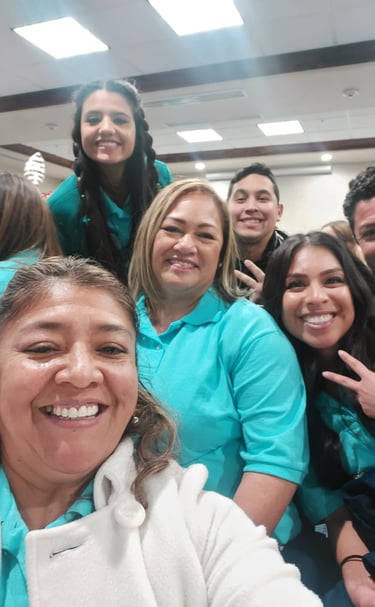 Smiling team members in teal shirts posing for a group selfie during a corporate event.