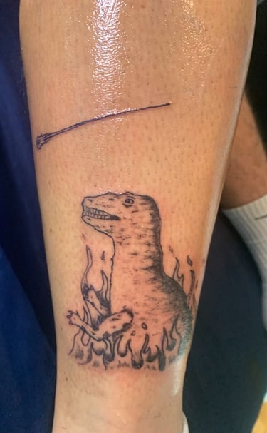 Tatouage dans un style enfantin assumé d'un dinosaure au milieu des flammes par a2c tattoo à Challes
