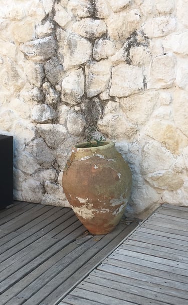itahome Rustic terracotta clay amphora jar on a wooden deck against a natural white stone wall.