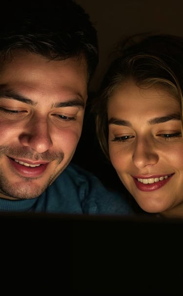 A smiling couple watching a movie on a tablet in a dark room.