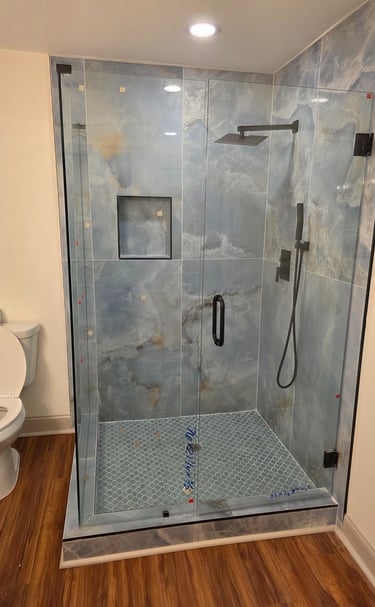 Modern bathroom featuring a walk-in glass shower with blue marble tiles and a black rainfall showerhead.