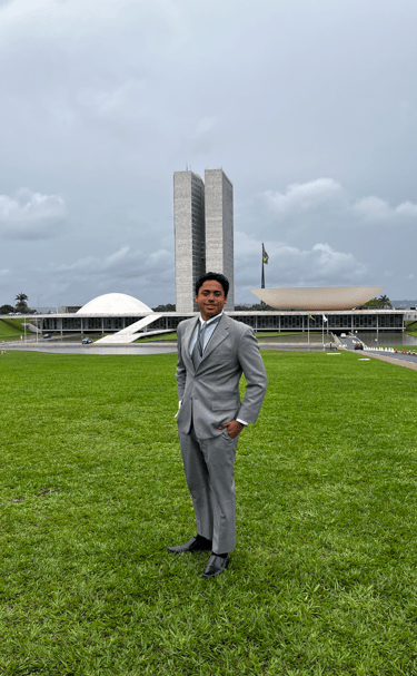 Jovem estudante vestido com terno cinza posando em frente ao Congresso Nacional em Brasília, represe
