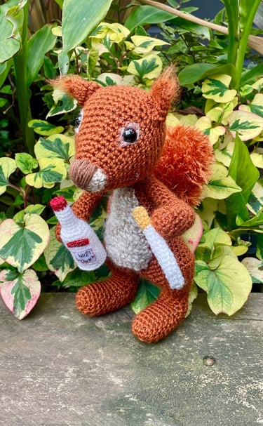 a crochet of a stuffed squirrel holding a bottle of vodka and a cigarette 