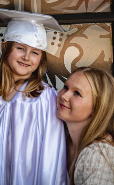 A proud Sister looking at her sibling wearing a white graduation cap and gown.