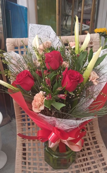 A bouquet of red roses, pink carnations, and white lilies in a vase with a red ribbon.