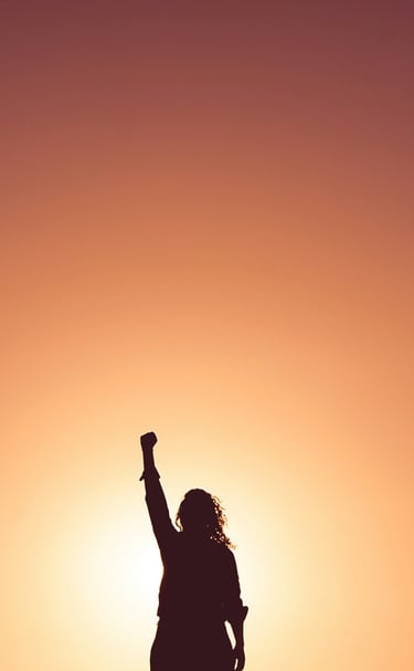 a person standing in front of a sunset with their hand raised