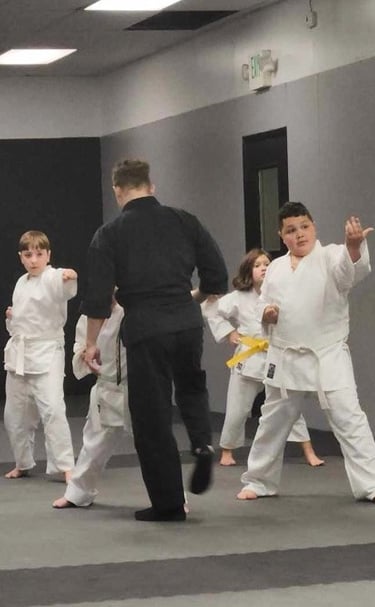 Young students in white uniforms practice karate moves during a martial arts class with a black-clad instructor.