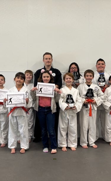 Martial arts instructor with students holding karate achievement certificates and trophies in a dojo.