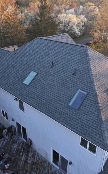 Aerial view of a suburban house featuring a new grey asphalt shingle roof with skylights.