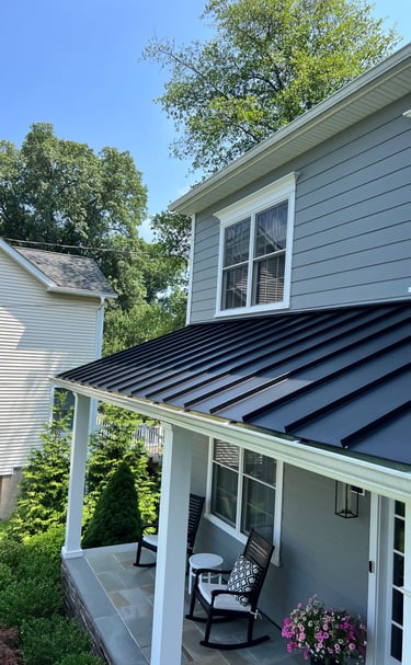 Modern black standing seam metal roof installed on a grey house porch with white columns.