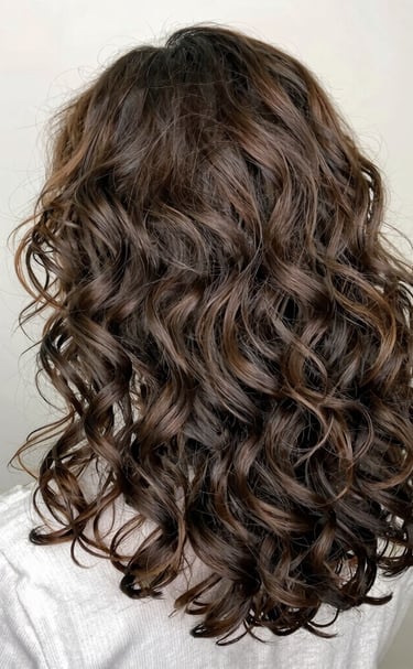 A joyful woman running fingers through her thick, lustrous hair in natural sunlight.