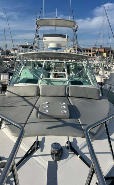 Luxury sportfishing boat bow featuring grey sunpad cushions and a tuna tower in a sunny marina.