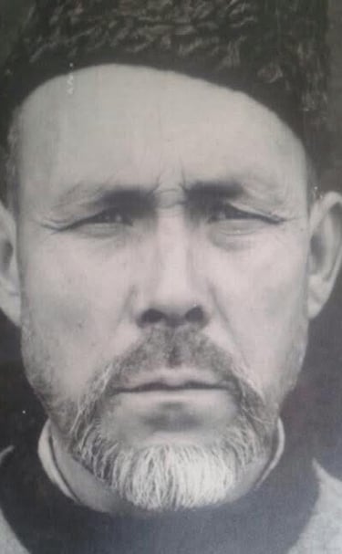 Vintage black and white portrait of an elderly man with a beard wearing a traditional hat.
