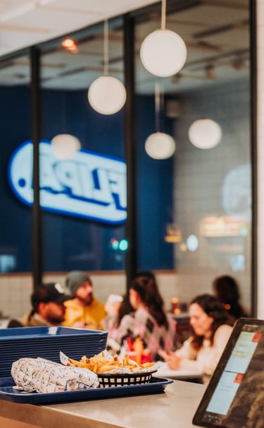 Clientes comiendo en Flipa con el logo iluminado reflejado en el cristal