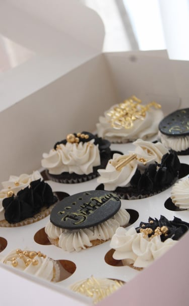 a box of cupcakes with white frosting and gold decorations