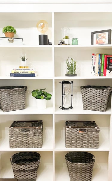 An organized bookshelf, decorated with plants and wicker baskets organized by Flawl