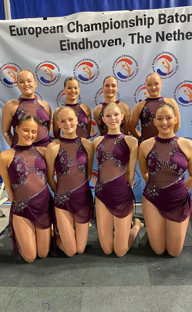 a group of young girls in purple dresses posing for a photo after a twirling competition