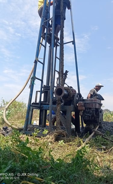 Construction workers using a manual rig for deep well drilling at a residential building site.