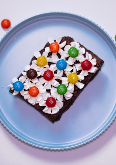 Brownie de chocolate tipo fudge cubierto con betún blanco y dulces M&M de colores sobre un plato