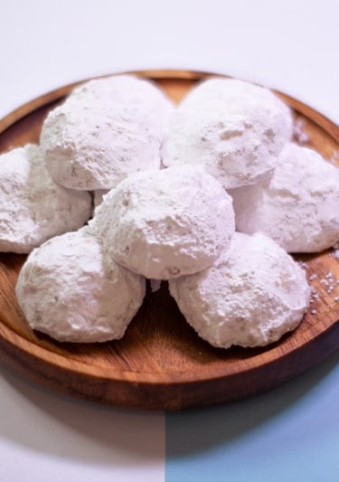 Plato de madera lleno de galletas redondas cubiertas de azúcar glass, conocidas como besos de nuez
