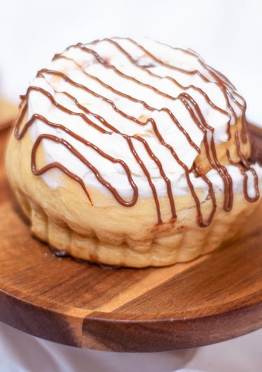 Rol de canela recién horneado con glaseado blanco y un chorrito de chocolate sobre un pedestal