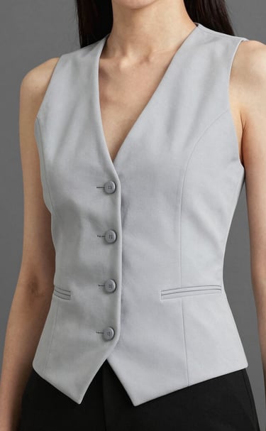 A woman wearing a tailored light grey button-up waistcoat vest with black trousers.