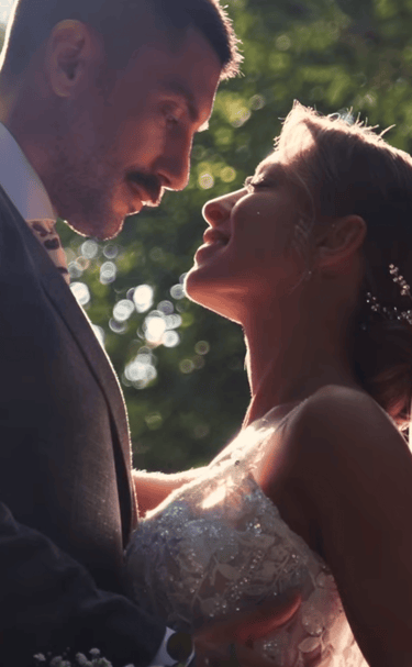A romantic bride and groom embrace during a sunlit outdoor wedding ceremony with natural bokeh.