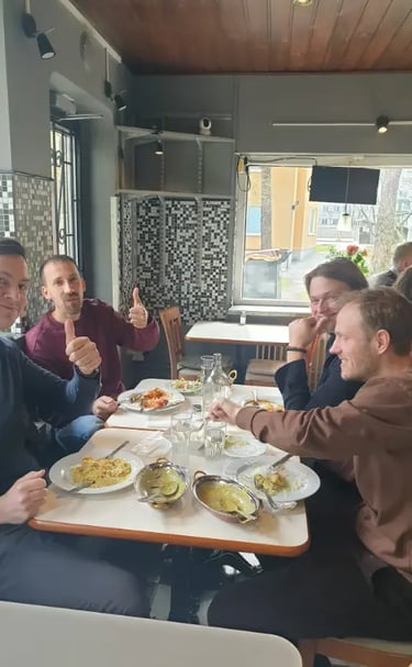 Four men enjoying a traditional Indian curry meal at a restaurant table with thumbs up.
