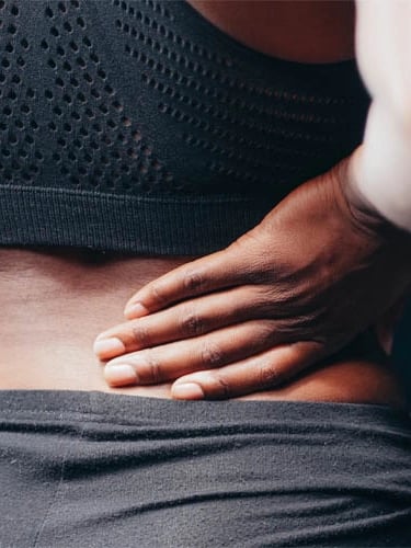 Mulher vestindo roupa de treino com dor na região lombar