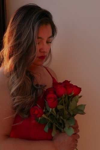 Una mujer con cabello largo y ondulado sosteniendo un ramo de rosas rojas con una iluminación calida