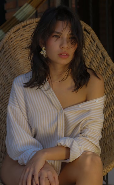 Joven mujer posando con una camisa medio hombro y pendientes dorados viendo el atardecer