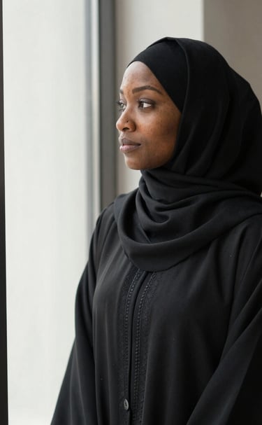 A woman smiling gently while adjusting her abaya sleeve by a window.