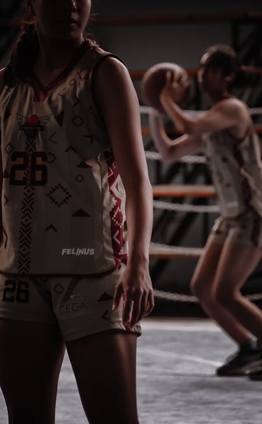 Female athlete wearing a custom patterned basketball jersey while a teammate shoots a ball in the background.