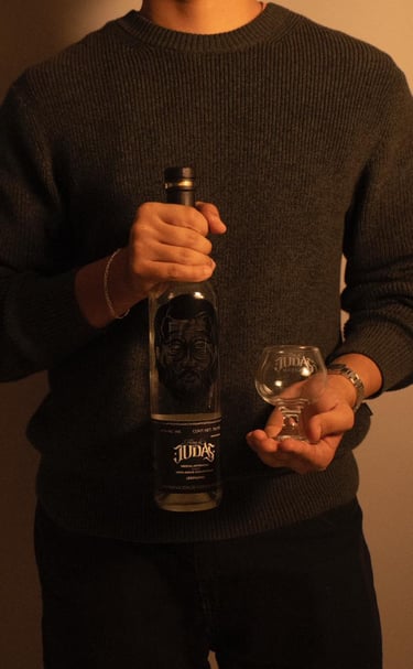 A person holding a bottle of Alma de Judas Mezcal and an empty tasting glass.