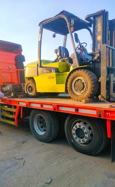A yellow Clark forklift secured on a red flatbed trailer for heavy machinery transport.