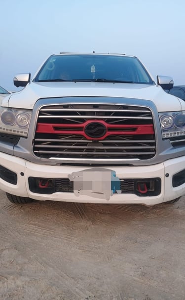 Front view of a white modified RAM pickup truck with a custom red and chrome grille parked on sand.